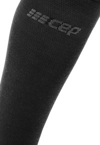 Calcetín deportivo negro con una textura suave y forma ajustada; presenta una sutil marca en gris a lo largo del costado.