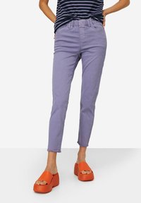 Pantalones de mezclilla lavanda con un diseño ajustado, que cuentan con una cintura elástica, dobladillo hasta el tobillo y puños deshilachados. Combinados con zapatos de plataforma naranjas.