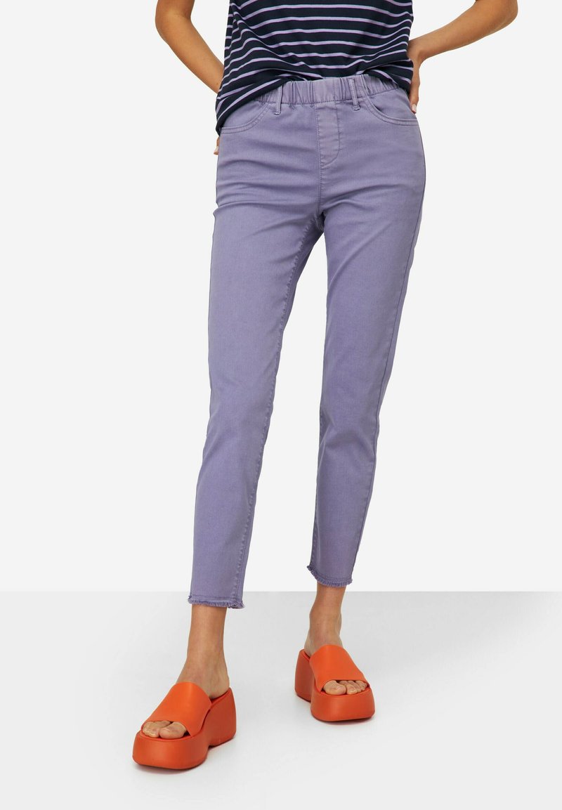 Pantalones de mezclilla lavanda con un diseño ajustado, que cuentan con una cintura elástica, dobladillo hasta el tobillo y puños deshilachados. Combinados con zapatos de plataforma naranjas.