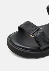 Czarne skórzane sandały z podwójnymi paskami, charakteryzujące się pikowaną teksturą i złotymi akcentami, okrągła podeszwa z teksturowanej czarnej gumy.