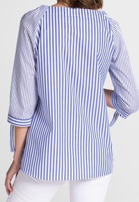 Chemise rayée bleue et blanche avec un col rond, des manches 3/4 et des poignets retroussés, fabriquée dans un tissu léger. Texture lisse.