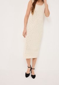 Robe midi en maille blanc cassé avec un col rond et un motif texturé ; associée à des escarpins noirs à brides à la cheville.