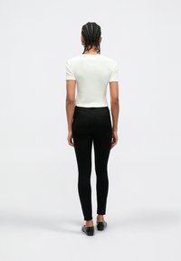 Bela kratka majica z rebrastim vzorcem in krojenim dizajnom, združena s črnimi oprijetimi kavbojkami. Postava stoji na nevtralni podlagi.