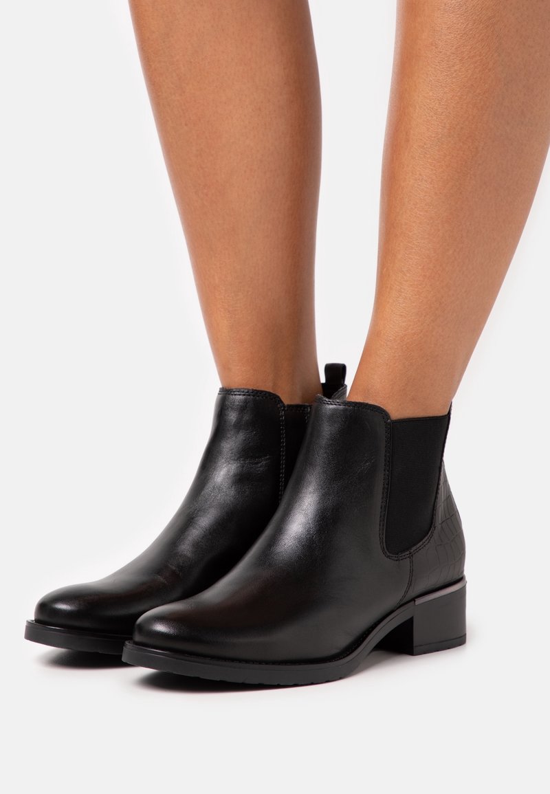 Botines de cuero negro con puntera redondeada, paneles laterales elásticos, parte trasera texturizada y un tacón bajo de bloque. Acabado liso en general.