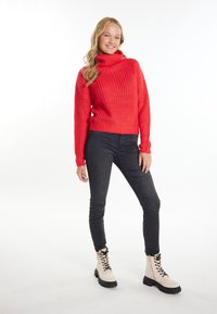 Roter Strickpullover mit Rollkragen aus strukturiertem Stoff, kombiniert mit schwarzen engen Jeans und beigefarbenen Schnürstiefeletten mit einer dicken Sohle.