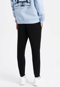 Lichtblauwe sweatshirt met grafische print op de achterkant, gecombineerd met zwarte joggingbroeken met elastische cuffs en zijzakken. Witte sneakers.