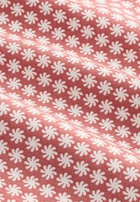 Tissu présentant un motif de formes semblables à des marguerites blanches sur un fond rose corail, avec une texture douce et lisse.