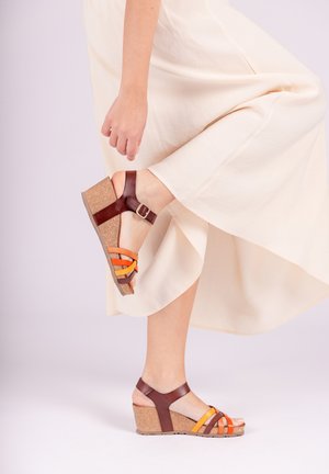 Bruine leren wedge sandalen met kurkzolen. De banden hebben oranje en gele accenten. Het ontwerp bevat een gesp en een open teen.