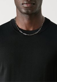 Czarny prążkowany t-shirt z okrągłym dekoltem, w zestawie ze srebrnym łańcuchem naszyjnym z wydłużonymi owalnymi ogniwami.