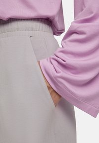 Lichtpaarse langetermijn top met gathered manchetten, gecombineerd met lichtgrijze broek met een elastische tailleband en zijzakken.
