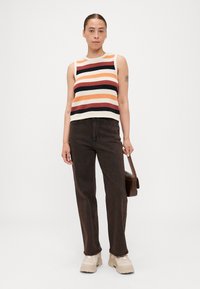 Top in maglia a righe nei colori crema, arancione, nero e rosso. Abbinato a jeans dritti marrone scuro e sneakers chunky beige. Borsa marrone come accessorio.