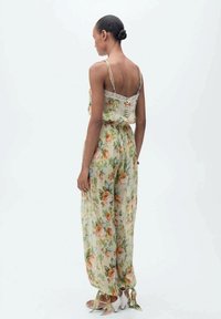 Floral jumpsuit with spaghetti straps, light fabric in green and orange hues, lace trim at the neckline, and tied cuffs at the ankles.