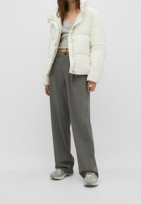 Dunjakke i off-white med en kort silhuet og trykknapper, stylet med grå vidde bukser og grå sneakers.