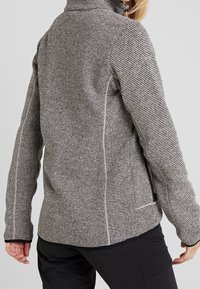 Chaqueta de forro polar con cuello alto, con un patrón a rayas en blanco y negro, ajuste ceñido y un bolsillo lateral con cremallera. Acabado texturizado.