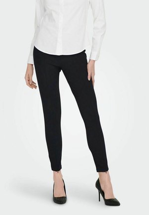 Black tailored pants with a slim fit, featuring a zip detail at the ankle. Worn with a white button-up shirt and black high heels.