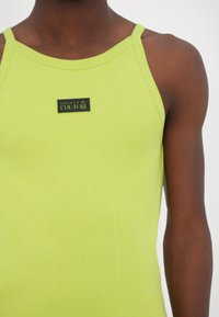 Limegrønn ribbet tanktop med tynne stropper, med en svart logo-plakett som sier "VERSACE JEANS COUTURE" på fronten.