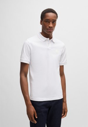 White polo shirt in a soft fabric with a collared neckline, three-button placket, and a small logo on the chest. Pairing with dark jeans.