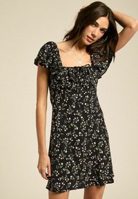 Abito nero a fiori con maniche corte a balze, caratterizzato da un décolleté quadrato e un corpetto aderente con orlo svasato. Piccole fantasie di fiori rosa e verdi.