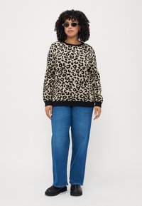 Leopardmønstret genser i beige og svart, med lange ermer og ribbestrikket kant. Kombinert med blå rettleggsjeans og svarte slip-on sko.