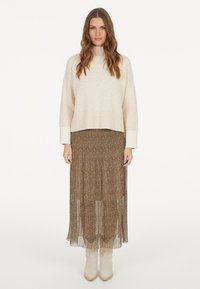 Cremfarbener Strickpullover mit hohem Kragen, kombiniert mit einem braunen, plissierten Rock mit einem dezenten Leopardenmuster und beigen Knöchelstiefeln.