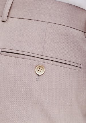 Jasnobeżowe spodnie z teksturowanej tkaniny, z tylnią kieszenią zapinaną na guzik oraz subtelnymi przeszyciami wzdłuż krawędzi kieszeni.