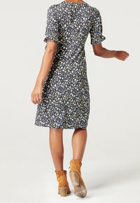 Svart blommig klänning med korta puffärmar, prydd med vita, gula och blå blommor. Den har en figursydd överdel och en utsvängd fåll.