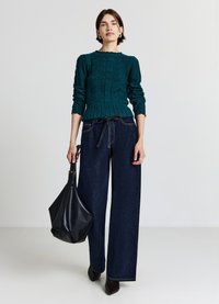 Maglione lavorato a maglia color teal con un design testurizzato e orlo a coste, abbinato a pantaloni a gamba larga in denim scuro con vita alta e una borsa a tracolla nera.