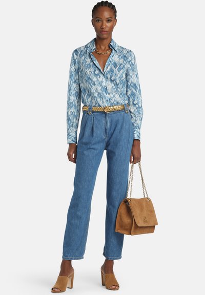 Svetlomodrá blúzka so vzorom a golierom, modré rifle s vysokým pásom, kožené sandále s hrubým podpätkom a hnedá semišová kabelka cez rameno.