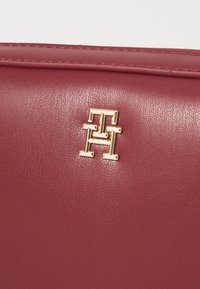 Burgunderfarbene Lederhandtasche mit einem goldenen Logo-Highlight, glatter Textur, rechteckiger Form und dezenten Nähten.