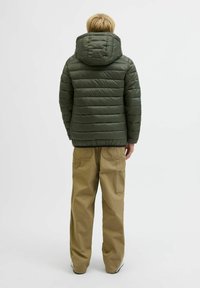Grön puffjacka med horisontell quiltning, huva och svart fåll, matchad med beige cargobyxor med sidofickor och lös passform.