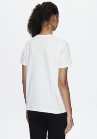 T-shirt en coton blanc à manches courtes, avec un col rond classique et une coupe droite. Couture visible et texture lisse et unie.