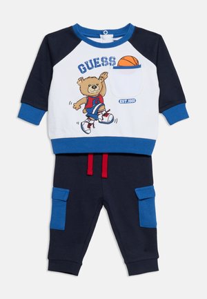 Zweiteiliges Outfit für Kleinkinder mit marineblauen und blauen Hosen, weißem und marineblauem Sweatshirt mit einem Bären, der Basketball spielt, und einer Basketball-Grafik auf der Tasche.
