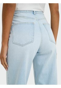 Ανοιχτό μπλε ψηλόμεσες τζίν με χαλαρή εφαρμογή. Χαρακτηριστικά περιλαμβάνουν πίσω τσέπες, ορατές ραφές και λεία υφή τζιν.