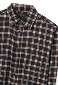 Camicia a quadri nera e beige con colletto, chiusura con bottoni e tessuto morbido. Presenta motivi a quadri orizzontali e verticali.