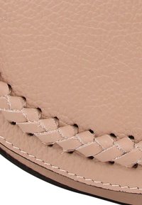 Lichtroze leer met een textuur, voorzien van een gevlochten rand en contrasterende witte stiksels, die het gedetailleerde vakmanschap benadrukken.