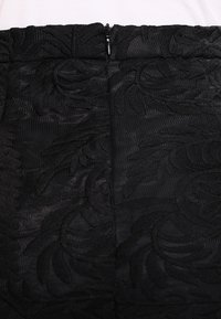 Černá sukně s texturovaným květinovým vzorem, vertikálním žebrováním a centrálním zipovým zapínáním na zadní straně. Hladký povrch látky.