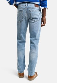 Jeans en denim bleu clair avec une coupe droite, cinq poches, un délavage subtil et une étiquette en cuir marron à l'arrière de la taille.
