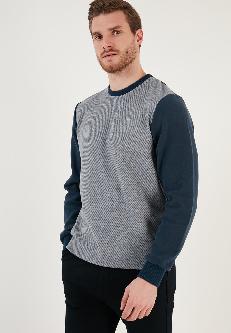 Felpa in misto cotone con corpo grigio texturizzato, maniche blu navy e colletto e polsini a costine. Vestibilità classica con dettagli minimi.