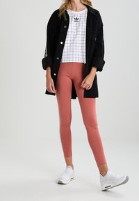 Svart oversized jacka, vit rutig crop top med logotyp, rosa leggings och vita sneakers. Texturerad tyg och kontrasterande färger.