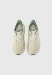 Beige Laufschuhe mit einem strukturierten Strick-Obermaterial, grünen Akzenten am Kragen und einer gepolsterten Sohle. Verfügt über Schnürsenkel und ein Markenlogo auf der Zunge.