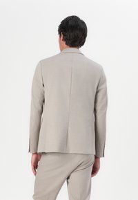 Light beige tailored suit jacket with a structured design, single back vent, and smooth texture. Features matching fabric trousers.