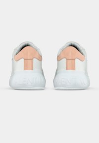 Λευκά αθλητικά παπούτσια με λεπτομέρεια σουέτ σε ροδακινί απόχρωση στη φτέρνα. Ελαστική σόλα με την ανάγλυφη επιγραφή "VALENTINO" στο πίσω μέρος. Λείο υλικό δέρματος.