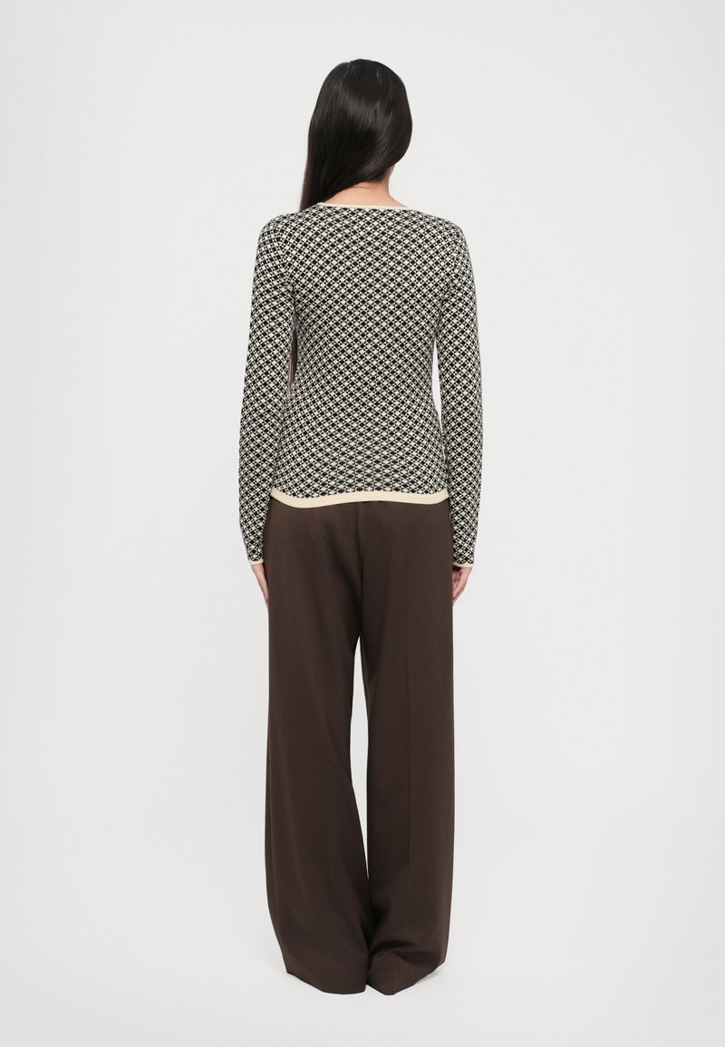 Langarmtop in zwart-wit geometrisch patroon, gecombineerd met losse bruine broeken. Soepele stof, ontspannen silhoeët.