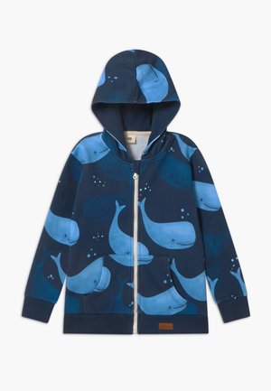 Mørkeblå hættetrøje med lynlås foran, prydet med et hvalemønster i forskellige blå nuancer og kontrasterende syninger.