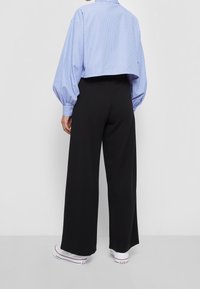 Cropped blue and white striped shirt with balloon sleeves, paired with high-waisted black wide-leg trousers and white sneakers.