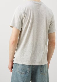 Šedé vřesové tričko vyrobené z měkké bavlny, s krátkým rukávem a kulatým výstřihem, s volným střihem a postranním švem pro větší pohyblivost.