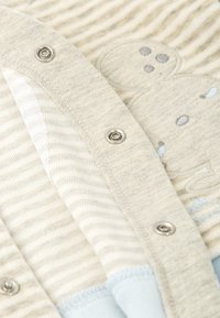 Cardigan gris claro con un patrón a rayas, botones de presión plateados y una textura suave. Diseño notable de oso en gris claro con acentos azules.
