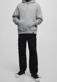 Szara bawełniana bluza z kapturem i kieszenią z przodu, zestawiona z czarnymi spodniami cargo z bocznymi kieszeniami i luźnym krojem. Czarne sneakersy.