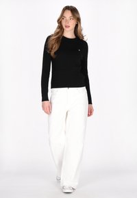 Zwarte ribgebreide trui met lange mouwen en een ronde halslijn, gecombineerd met witte wijde broek en witte sneakers. Geen zichtbare patronen.