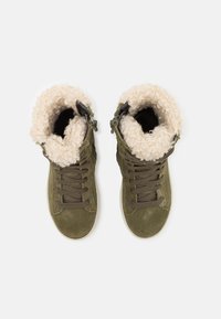 Botines de ante verde con forro de pelaje sintético, cierre con cordones en la parte frontal y suela de goma texturizada. El cuello está forrado con forro polar de color crema.